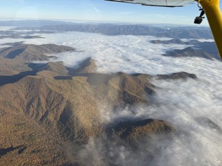 Undercast filling the valleys below, ridges standing out of the cloud, wing and camera mount in frame